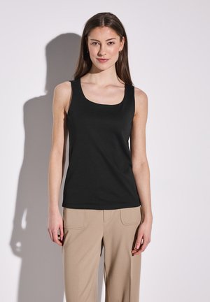Schwarzes Tanktop mit rundem Halsausschnitt, aus einem glatten, dehnbaren Stoff gefertigt. Kombiniert mit beigen, weit geschnittenen Hosen, die ein minimalistisches Design zeigen.