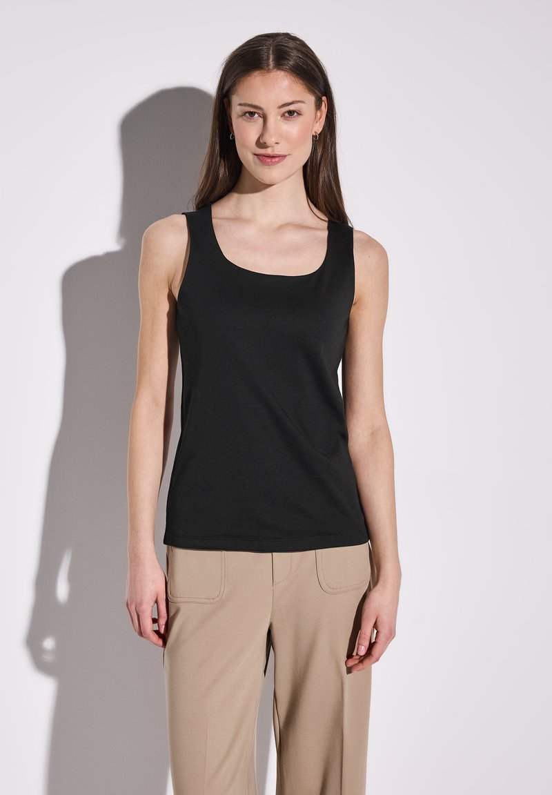Schwarzes Tanktop mit rundem Halsausschnitt, aus einem glatten, dehnbaren Stoff gefertigt. Kombiniert mit beigen, weit geschnittenen Hosen, die ein minimalistisches Design zeigen.