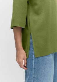 Ljust grönt, texturerat stickat linne med korta ärmar och sidofickor, kombinerat med löst sittande blå denimjeans.