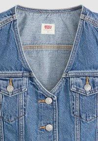 Top sans manches en denim bleu clair avec un décolleté en V, deux poches poitrine, boutons en argent et détails de couture orange contrastants.