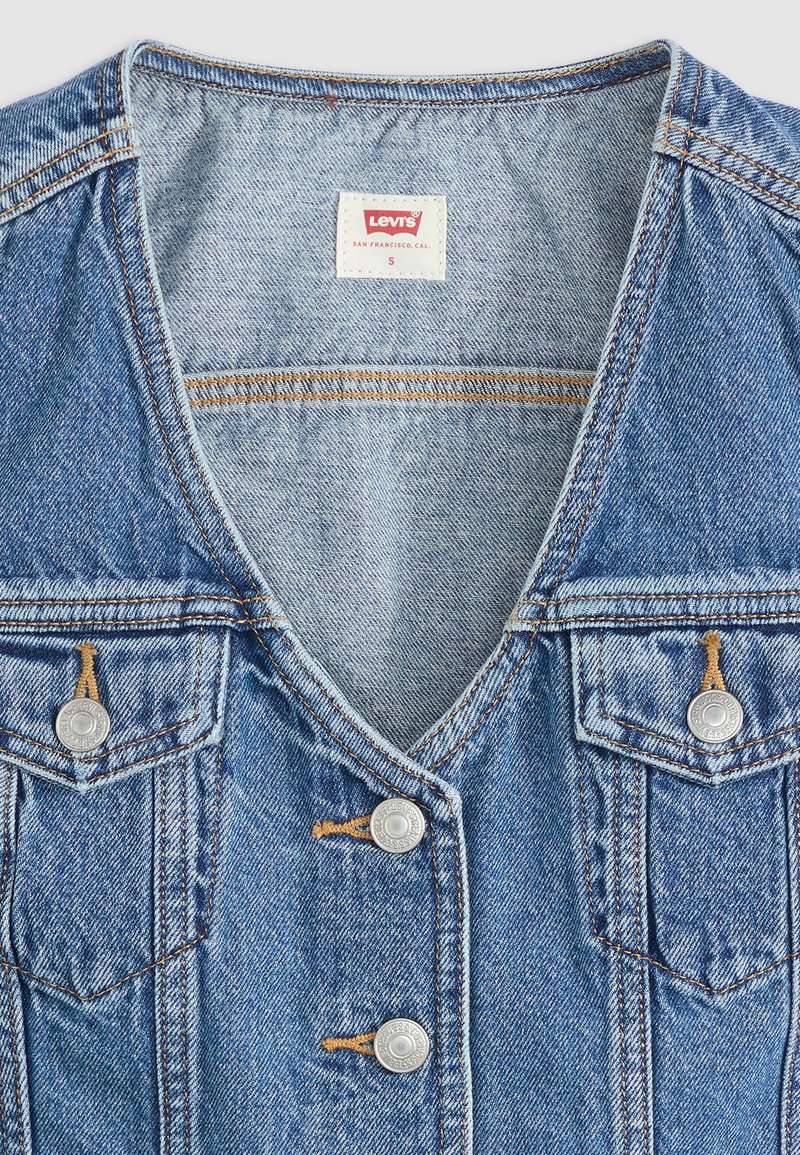 Hellblaues Denim-Top ohne Ärmel mit V-Ausschnitt, zwei Brusttaschen, silbernen Knöpfen und kontrastierenden orangen Nähdetails.