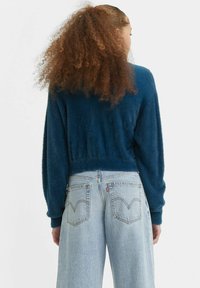 Pull cropped et moelleux, bleu marine, avec des manches longues et un tissu texturé. Assorti à un jean large bleu clair avec poches arrière et détails de couture.