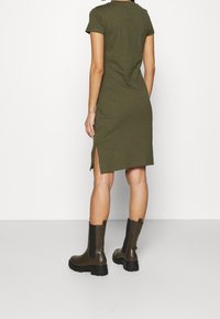 Oliwkowa, krótko rękawowa sukienka z bocznymi rozcięciami, dopasowany fason, wykonana z bawełnianej mieszanki. W połączeniu z grubymi, brązowymi botkami za kostkę.