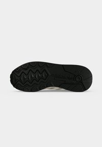 Μαύρη σόλα παπουτσιού Adidas με γεωμετρικό πέλμα και ορατό λογότυπο σε απλό φωτεινό φόντο.