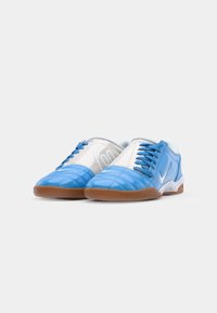 Blaue und weiße Sportschuhe mit glatter Oberfläche, ausgestattet mit einer Gummisohle, Schnürsenkeln und einem silbernen Swoosh-Logo an der Seite.