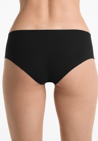 Zwarte bikini onderkant met een lage taille en zachte stof. Naadloze randen en minimale bedekking benadrukken een slank silhouet.