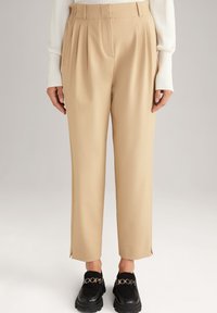 Beżowe spodni z zakładkami, lekko zwężające się w kostce, z bocznymi rozcięciami. W zestawieniu z masywnymi czarnymi loafersami z akcentami logo.
