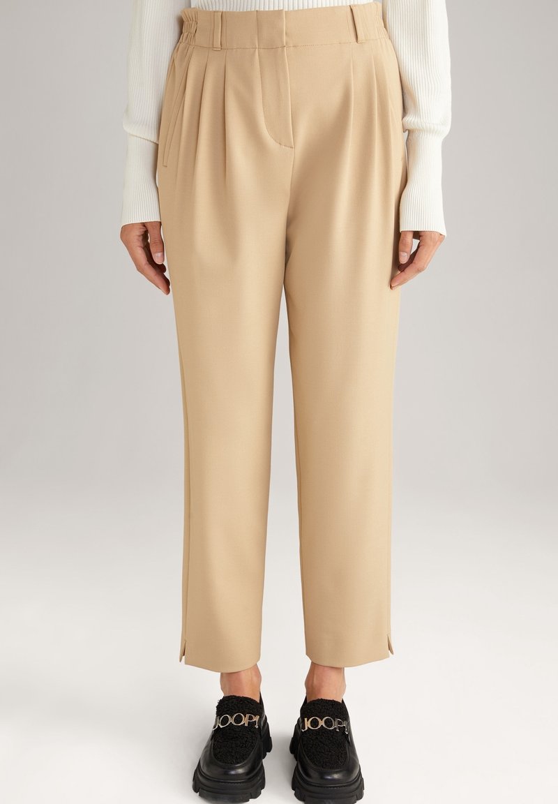 Beżowe spodni z zakładkami, lekko zwężające się w kostce, z bocznymi rozcięciami. W zestawieniu z masywnymi czarnymi loafersami z akcentami logo.