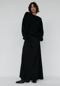 Czarny, oversize'owy, dziany sweter z okrągłym dekoltem, zestawiony z długą czarną spódnicą. Gładka faktura i prosty design. Czarne botki za kostkę.