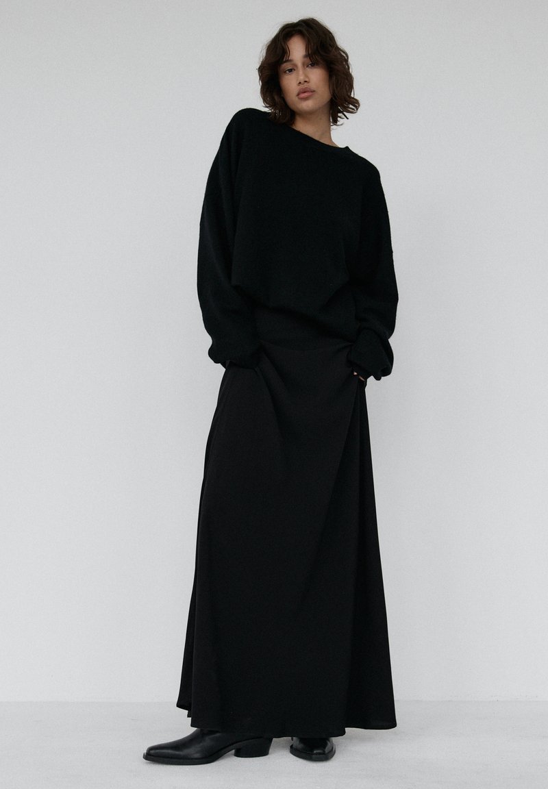 Czarny, oversize'owy, dziany sweter z okrągłym dekoltem, zestawiony z długą czarną spódnicą. Gładka faktura i prosty design. Czarne botki za kostkę.