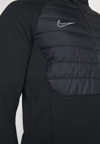Czarna bluza Nike z zamkiem błyskawicznym na ćwierć, z pikowaną teksturą na klatce piersiowej oraz gładkim materiałem na rękawach i bokach.