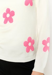 White knitted sweater featuring bright pink flower patterns, with a ribbed hem and cuffs. The design has a smooth, soft texture.