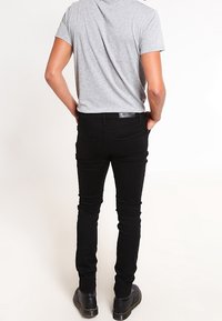 Jeans negros de corte ajustado con una textura suave y diseño de cinco bolsillos, combinados con una camiseta gris de manga corta y calzado negro.