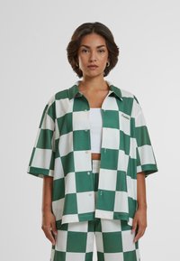 Camicia a quadri verde e bianca con maniche corte, design con colletto, chiusura con bottoni e logo anteriore. Abbinata a pantaloni a quadri coordinati.