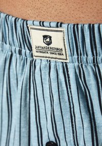 Helleblau gestrefter Stoff mit dünnen schwarzen Linien, elastischer Bund mit einem Etikett, das "JAN VANDERSTORM AUTHENTIC SINCE 1984" lautet.