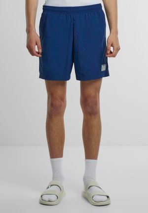 Mørkeblå shorts med elastisk midjebånd og sidelommer, med et lite merke på kanten. Glatt, lett stoff.