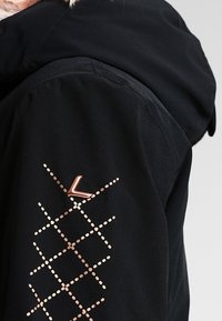 Schwarze Jacke mit Kapuze, ausgestattet mit einem diagonalen, roségoldenen Punktmuster und einem metallic Akzent am Ärmel. Glatte Textur, modernes Design.