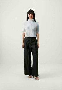 Light blue ribbed turtleneck short-sleeve top paired with high-waisted black wide-leg trousers and light-colored open-toe heels.