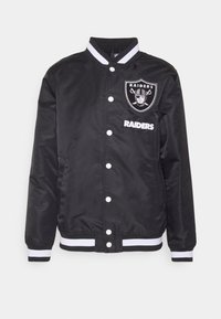 Černá bomber bunda se bílými pruhy na límci a rukávech. Obsahuje vyšitý logo Raiders a nápis. Vyrobena z lesklé látky se zapínáním na patentky.