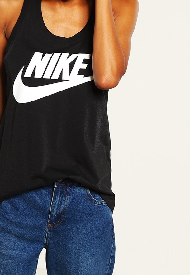 Černá bezrukávová tank top s velkým bílým logem Nike na přední straně; v kombinaci s modrými džíny, představující neformální vzhled.