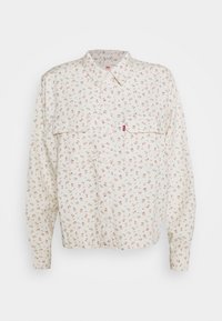 Chemise boutonnée fleurie couleur crème, ornée de petites fleurs roses, deux poches poitrine et un col classique. Confectionnée en tissu doux avec des manches longues.