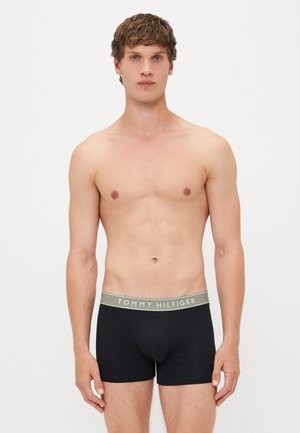 Schwarze Boxershorts mit einem grauen Bund, der mit dem Logo "TOMMY HILFIGER" versehen ist. Glatte Textur, enganliegendes Design und mittellange Beine bis zur Mitte des Oberschenkels.