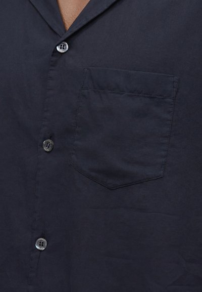 Κοντινό πλάνο ενός μπλε σκούρου πουκάμισου με κουμπιά που δείχνει τρία κουμπιά και μια τσέπη στο στήθος στην αριστερή πλευρά.