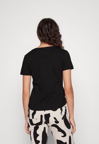 Czarna koszulka z krótkim rękawem i okrągłym dekoltem, wyświetlona z tyłu, w połączeniu z kremowymi spodniami z czarnym abstrakcyjnym wzorem.