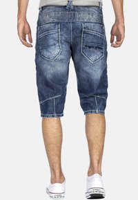 Shorts en denim capri de couleur bleu foncé délavé avec une coupe droite. Dotés de détails de poches cousus et d'un logo sur la ceinture.