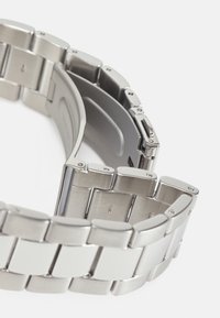 Banda de reloj de metal plateado con eslabones entrelazados, que presenta un acabado pulido y un mecanismo de cierre seguro. Texturizada para mayor comodidad y durabilidad.