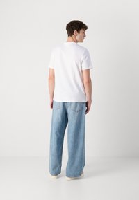 Weißes Kurzarm-T-Shirt und hellblaue übergroße Jeans. Die Jeans haben einen bequemen Schnitt und sichtbare Hintertaschen.