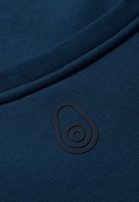 Sudadera de color azul marino con una textura suave. Logo negro destacado con un patrón circular en la parte delantera. Detalle de cuello acanalado.