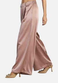 Satinweite Hosen aus weichem Pink mit glatter Textur, hoher Taille und Seitentaschen, kombiniert mit beigen Absatzschuhen.