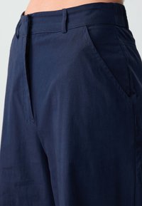 Pantalons navy en tissu léger, dotés d'une fermeture éclair, de poches avant et d'une texture lisse avec une coupe ajustée.