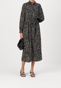Czarna midi sukienka w paisley, z długimi rękawami, z przodem zapinanym na guziki oraz paskiem w talii. Połączona z czarną torebką i sandałami.