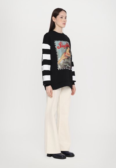 Black sweatshirt with a colorful graphic print featuring a seated figure. It has bold black and white striped sleeves and a relaxed fit.