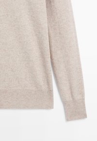 Lichtbeige gebreide trui met een mouw en onderlichaamssectie die een zachte textuur en ribbelmanchetten en onderrand laat zien.