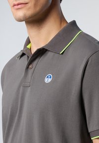 Polo grigio con tessuto testurizzato, rifinitura del colletto verde chiaro e un logo rotondo sul petto. Presenta una chiusura con tre bottoni.