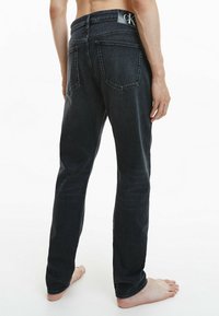 Svarta denimjeans med rak passform, med en märkestagg på midjebandet och två bakfickor, visade från baksidan.