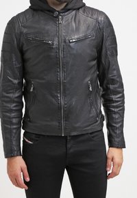 Schwarze Lederjacke mit einem Frontreißverschluss, subtilen Schulterpolsterungen und zwei aufgesetzten Brusttaschen mit Reißverschluss. Sanfte Textur mit einer taillierten Passform.