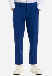 Blauwe op maat gemaakte broek met een gladde textuur, voorzien van zijzakken, voorkruisplooien en een slim fit, gecombineerd met witte sneakers.