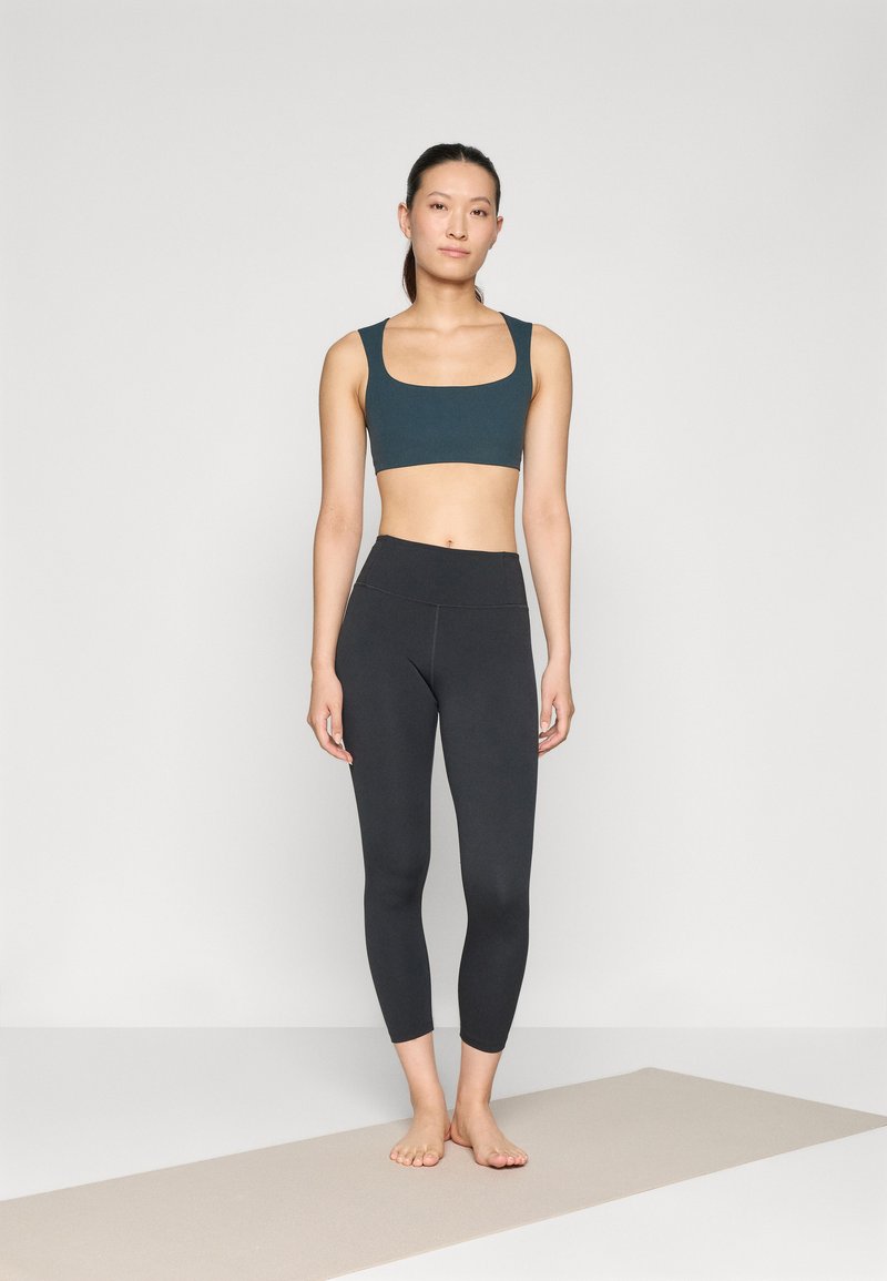 Atletische outfit met een donkere teal crop top met brede banden en zwarte full-length leggings. Glad textuur, aansluitend ontwerp.