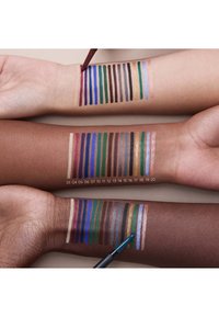 Swatches of various colored cosmetics on three arms, showcasing differing skin tones. Each arm displays horizontal lines of diverse shades and finishes.