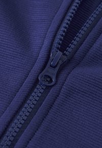 Marineblaue, mit Reißverschluss versehene Jacke aus strukturiertem Stoff mit feiner Rippung. Der Reißverschluss hat einen glatten Ziehgriff für einfaches Öffnen und Schließen.