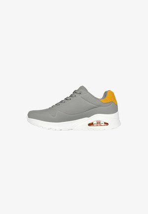 Graue Sportschuhe aus glattem Material, mit einer weißen Sohle und einem gelben Akzent an der Ferse. Verfügt über perforierte Details und Schnürsenkel.