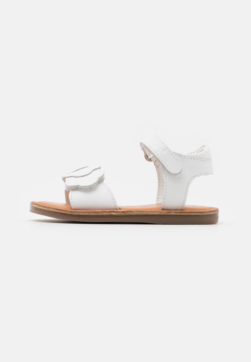 Hvite skinnsandaler med blomstermønster, justerbare stropper, flat gummisåle, og lys brun såle. Sideperspektiv.