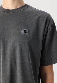 Gray cotton t-shirt with a crew neckline and short sleeves. Features a sewn-on rectangular Carhartt tag on the left chest.