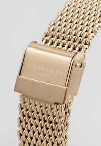 Goudtint mesh-horloge met een metalen sluiting met het geperste merk "LIEBESKIND BERLIN." Gelaagde schakels creëren een flexibele ontwerp.
