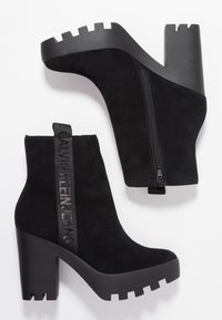 Mustat mokkanahka nilkkurit, joissa on korkea, paksu korko, sivuva zipper ja br�ändätty kangasketju. Varustettu tekstuurilla mustalla alustalla.