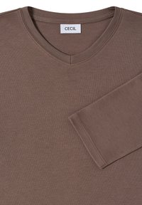 Chemise marron à col en V à manches longues avec une texture lisse et des coutures renforcées, comportant une étiquette indiquant "CECIL" au niveau de l'encolure.
